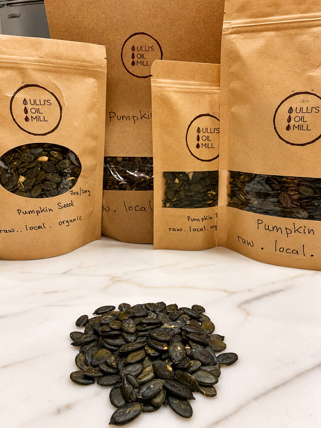 Kraft pouches of Ulli's organic raw Styrian pumpkin seeds beside a pile of seeds